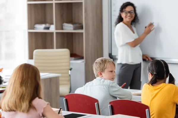 Blurred african american teacher writing on whiteboard near pupils in classroom — Stock Photo