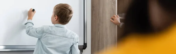 Vue arrière de l'écolier écrivant sur le tableau blanc pendant le cours, bannière — Photo de stock