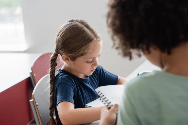 Blurred african american boy standing near schoolgirl in classroom — Stock Photo