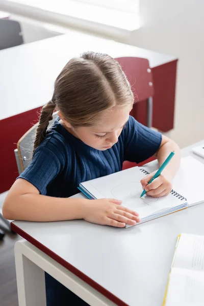 Écolière écrit dans un cahier pendant les cours à l'école — Photo de stock