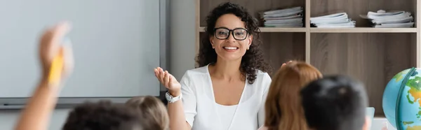 Enseignant afro-américain souriant pointant avec la main près des enfants flous, bannière — Photo de stock