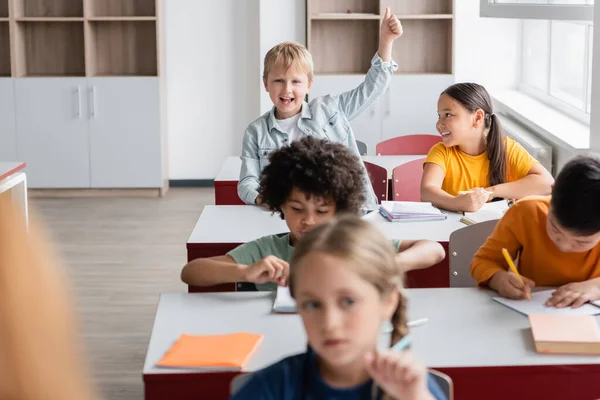 Fröhlicher Junge mit erhobener Hand, der im Unterricht den Daumen nach oben zeigt — Stockfoto