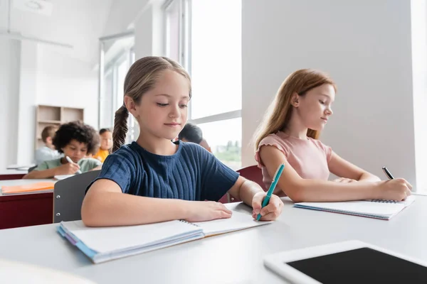 Multicultural children writing in notebooks during lesson — Stock Photo