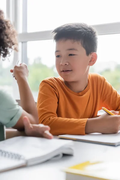 Verschwommener Junge zeigt mit Stift nahe asiatischer Klassenkameradin — Stockfoto