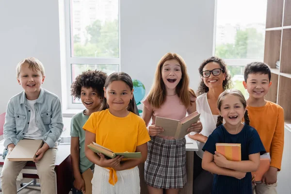 Aufgeregte multiethnische Schüler mit afrikanisch-amerikanischem Lehrer, der im Klassenzimmer in die Kamera blickt — Stockfoto