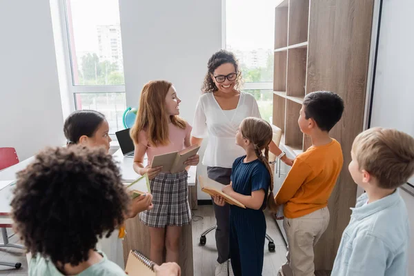 Multiethnische Schüler mit Büchern im Gespräch mit fröhlichen afrikanisch-amerikanischen Lehrern im Klassenzimmer — Stockfoto