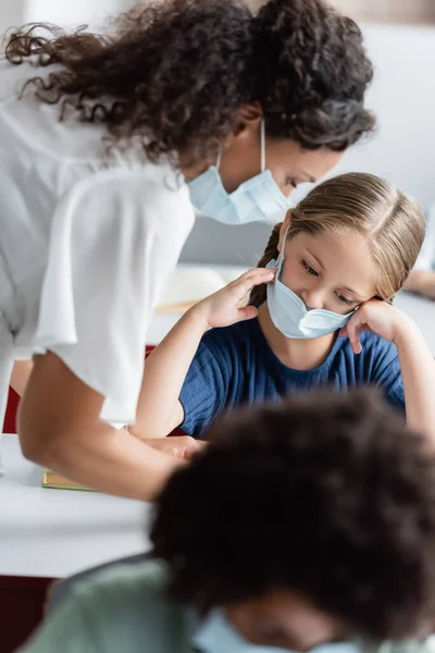 Africano americano insegnante in medico maschera aiutare ragazza durante lezione — Foto stock