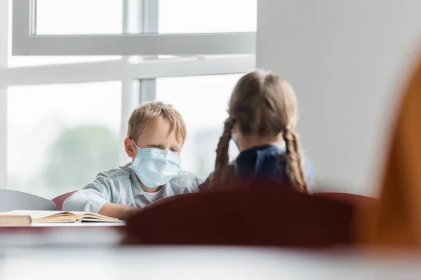 Школьник в медицинской маске рядом с размытой девушкой в классе — стоковое фото