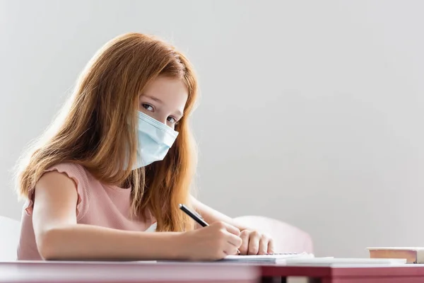 Studentessa in maschera medica scrittura durante la lezione di scuola — Foto stock