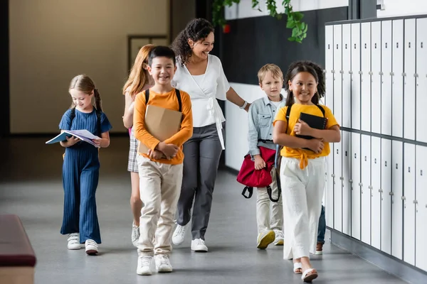Веселые дети прогуливаются по школьному коридору с веселым африканским учителем Америки — стоковое фото