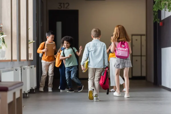 Escolares multiétnicos com mochilas e cadernos no corredor escolar — Fotografia de Stock