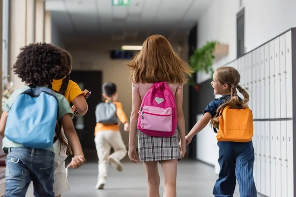 Vue arrière des élèves multiethniques avec des sacs à dos en cours d'exécution à l'école — Photo de stock