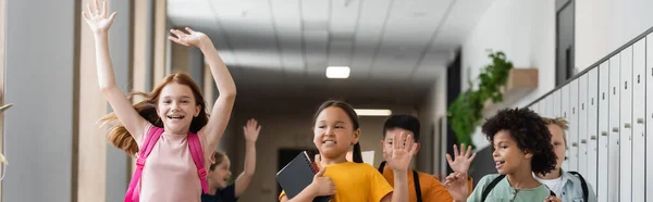 Cheerful multicultural children waving hands in school corridor, banner — Stock Photo