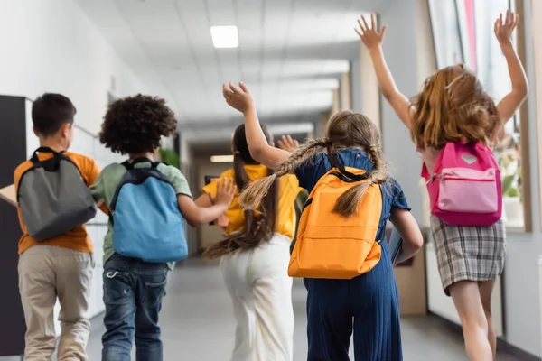 Vista trasera de los escolares multiétnicos corriendo en el pasillo escolar - foto de stock