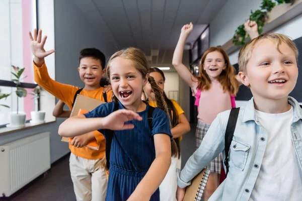 Eccitati compagni di classe multietnici che salutano le mani e mostrano un gesto vincente nella sala della scuola — Foto stock