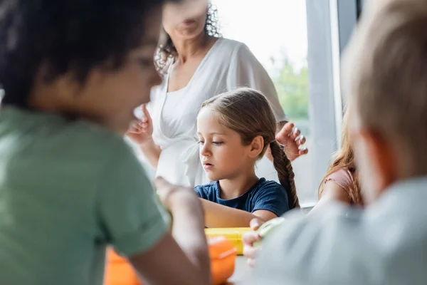 Selective focus of schoolgirl near blurred interracial kids and african american teacher — Stock Photo