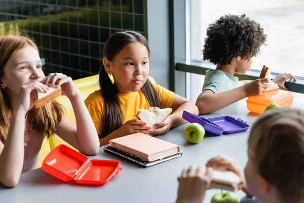 Niños multiétnicos almorzando en el comedor escolar - foto de stock
