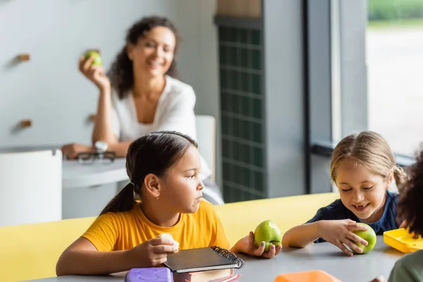 Verschwommene afrikanisch-amerikanische Lehrerin lächelt in der Nähe interrassischer Schulmädchen beim Mittagessen in einem Lokal — Stockfoto