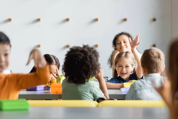 Excited multiethnic kids waving hands during lunch in school canteen — Stock Photo