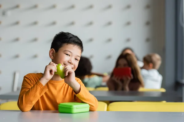 Gai asiatique garçon avec frais pomme sourire à caméra dans école manger — Photo de stock