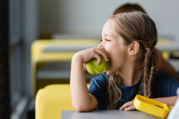 Estudante olhando embora enquanto comendo maçã na cantina da escola — Fotografia de Stock
