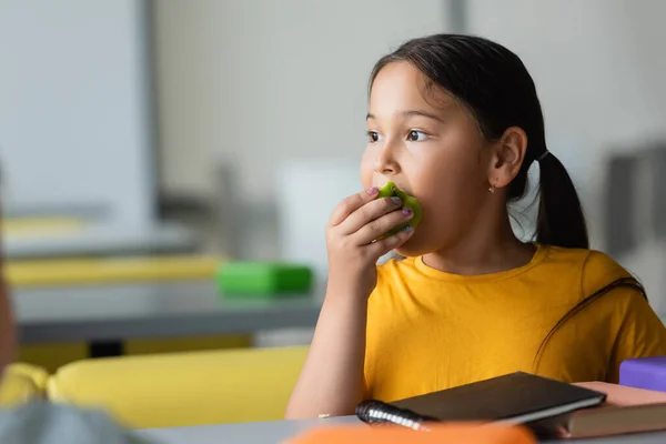 Ásia aluna comer maçã durante almoço pausa no escola restaurante — Fotografia de Stock