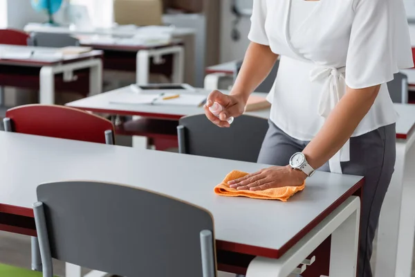 Partial view of african american teacher cleaning desk with sanitizer — Stock Photo