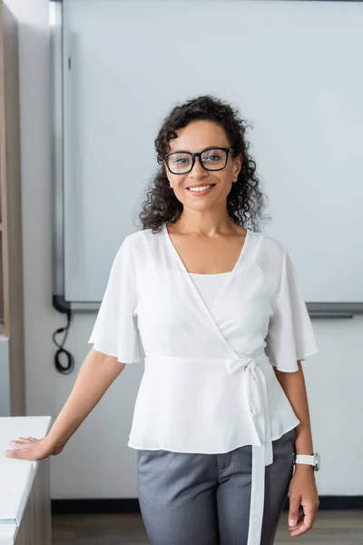 Pretty african american teacher smiling at camera in classroom — Stock Photo