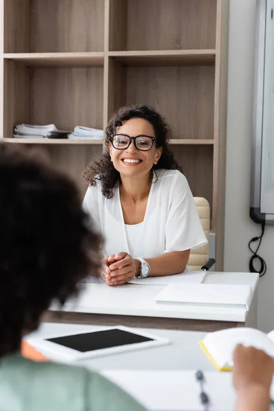 Cheerful teacher looking at african american boy on blurred background in classroom — Stock Photo