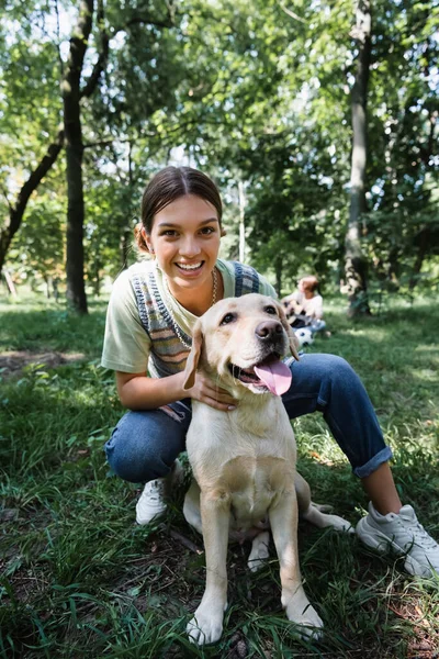 Cheerful teenager looking at camera near retriever in park — Stock Photo