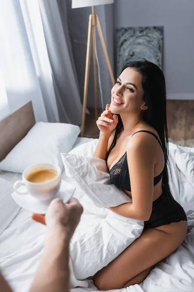 Blurred man holding cup of cappuccino near cheerful sexy woman in underwear — Stock Photo