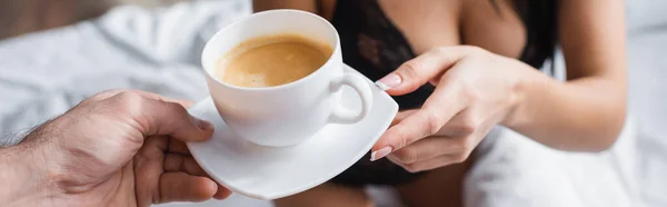 Abgeschnittene Ansicht eines verschwommenen Mannes mit einer Tasse Cappuccino in der Nähe einer verführerischen Frau im Schlafzimmer, Banner — Stockfoto