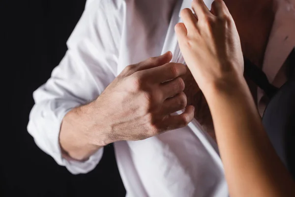 Recortado vista de la mujer desvestirse hombre en camisa blanca aislado en negro - foto de stock