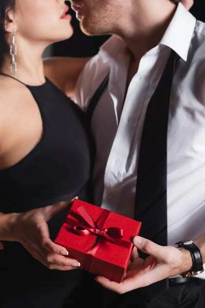 Partial view of man holding gift box and kissing with woman in dress — Stock Photo