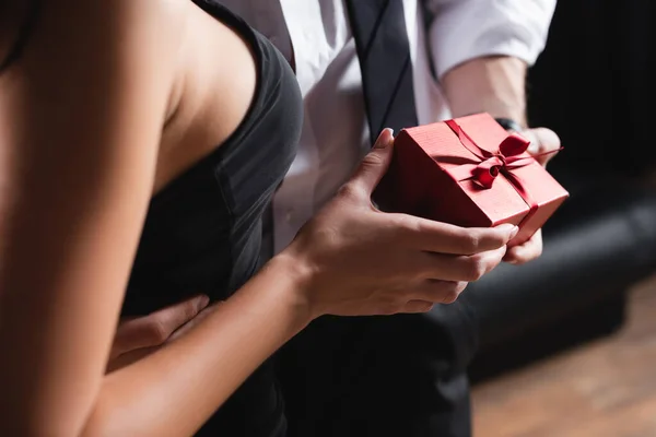 Vista parcial del hombre sosteniendo caja de regalo roja cerca de la mujer en vestido en negro - foto de stock