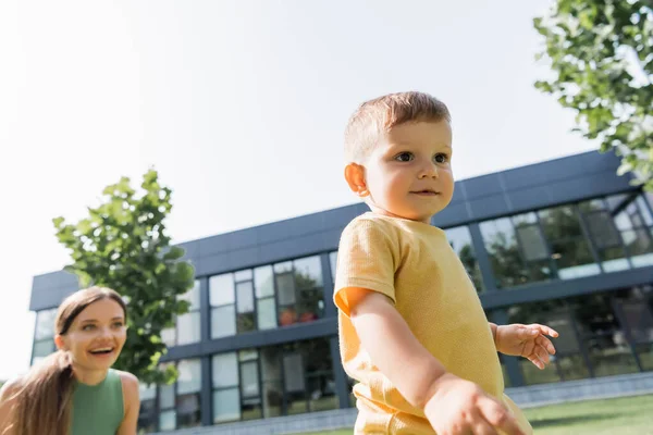 Niño pequeño caminando cerca borrosa feliz madre en el fondo - foto de stock