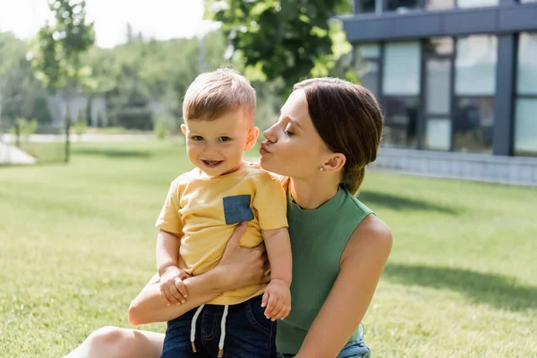 Junge Mutter küsst glücklich Kleinkind Sohn draußen — Stockfoto