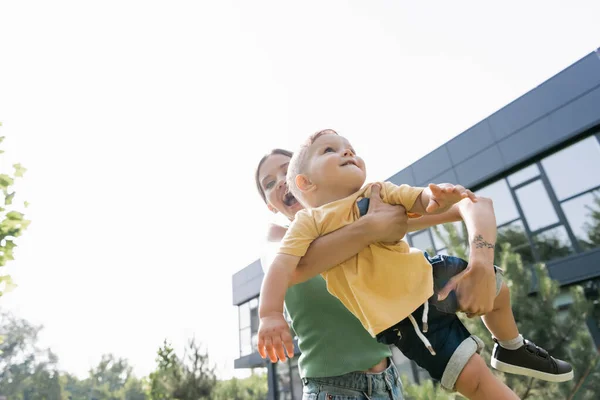 Low angle view of amazed young mother holding in arms smiling toddler son — Stock Photo