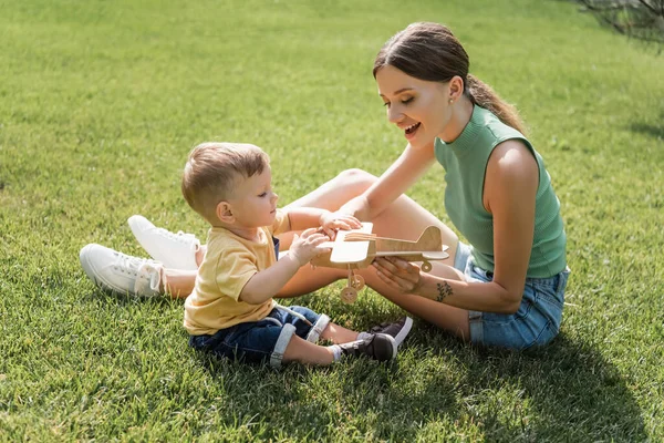 Alegre madre celebración juguete biplano cerca de niño hijo en la hierba - foto de stock