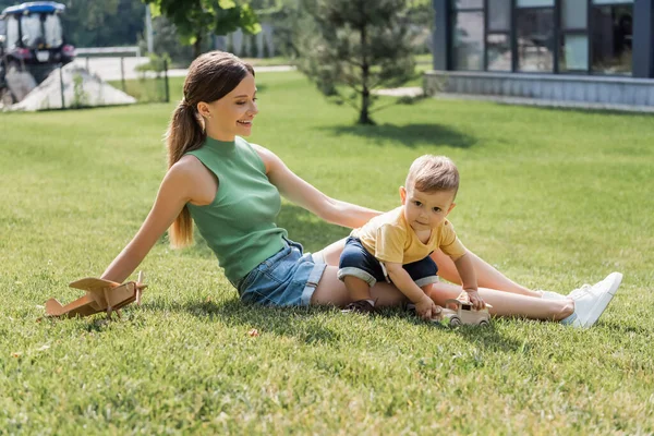 Happy young mother looking at cheerful toddler son playing on grass — Stock Photo