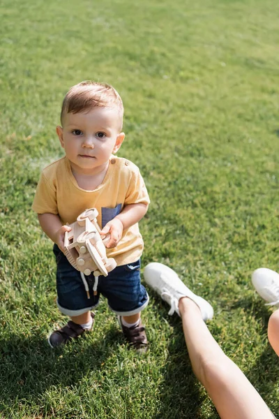 Bambino ragazzo in piedi su erba e tenendo giocattolo auto vicino alla madre — Foto stock