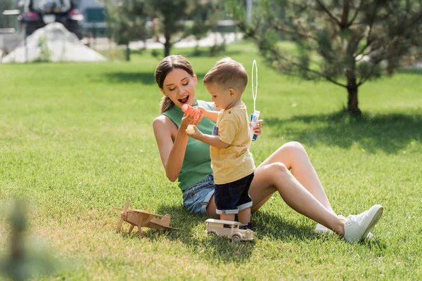 Amazed mother looking at toddler son pouring liquid with soap bubbles — Stock Photo