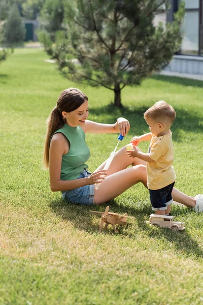 Joyful mother holding bubble wand near toddler son outside — Stock Photo