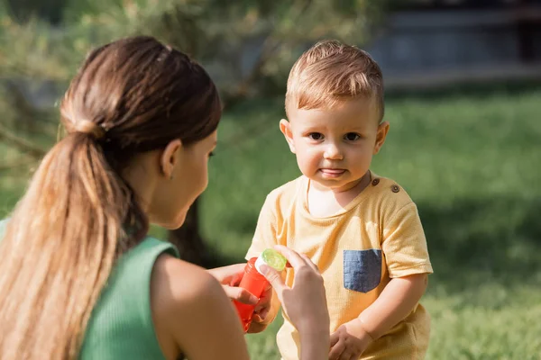 Розмита мати тримає пляшку і бульбашкову паличку біля хлопчика на вулиці — стокове фото