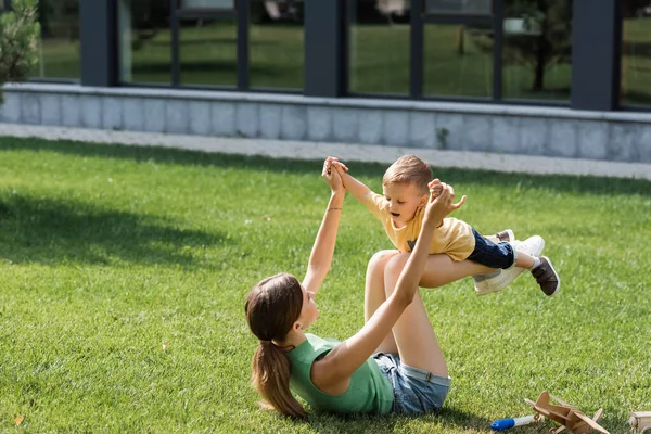 Mère couchée sur l'herbe et levant tout-petit fils — Photo de stock