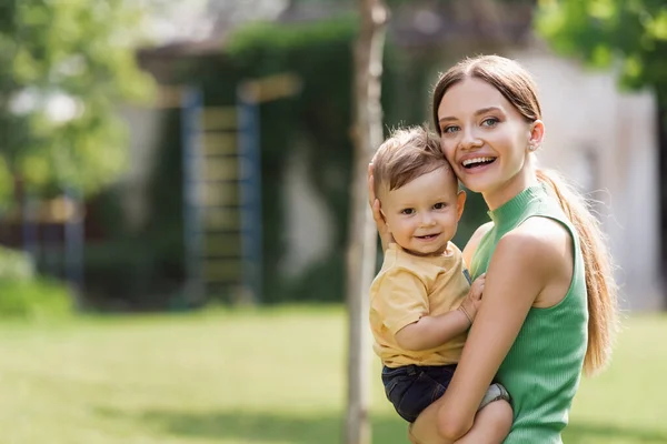 Emocionado y joven madre sosteniendo en brazos hijo pequeño — Stock Photo