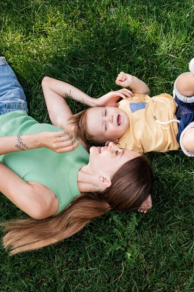 Top view of happy mother spending time with happy toddler son while lying on grassy lawn — Stock Photo