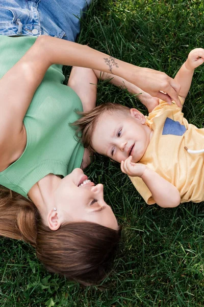 Vue de dessus de la mère gaie passer du temps avec fils tout-petit heureux tout en étant allongé sur l'herbe — Photo de stock