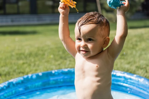 Cheerful toddler boy holding rubber toys above head outside — Stock Photo
