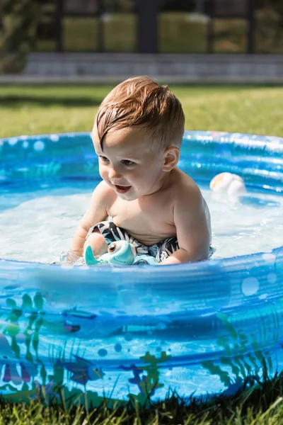Cheerful toddler boy sitting in inflatable pool with rubber toys — Stock Photo
